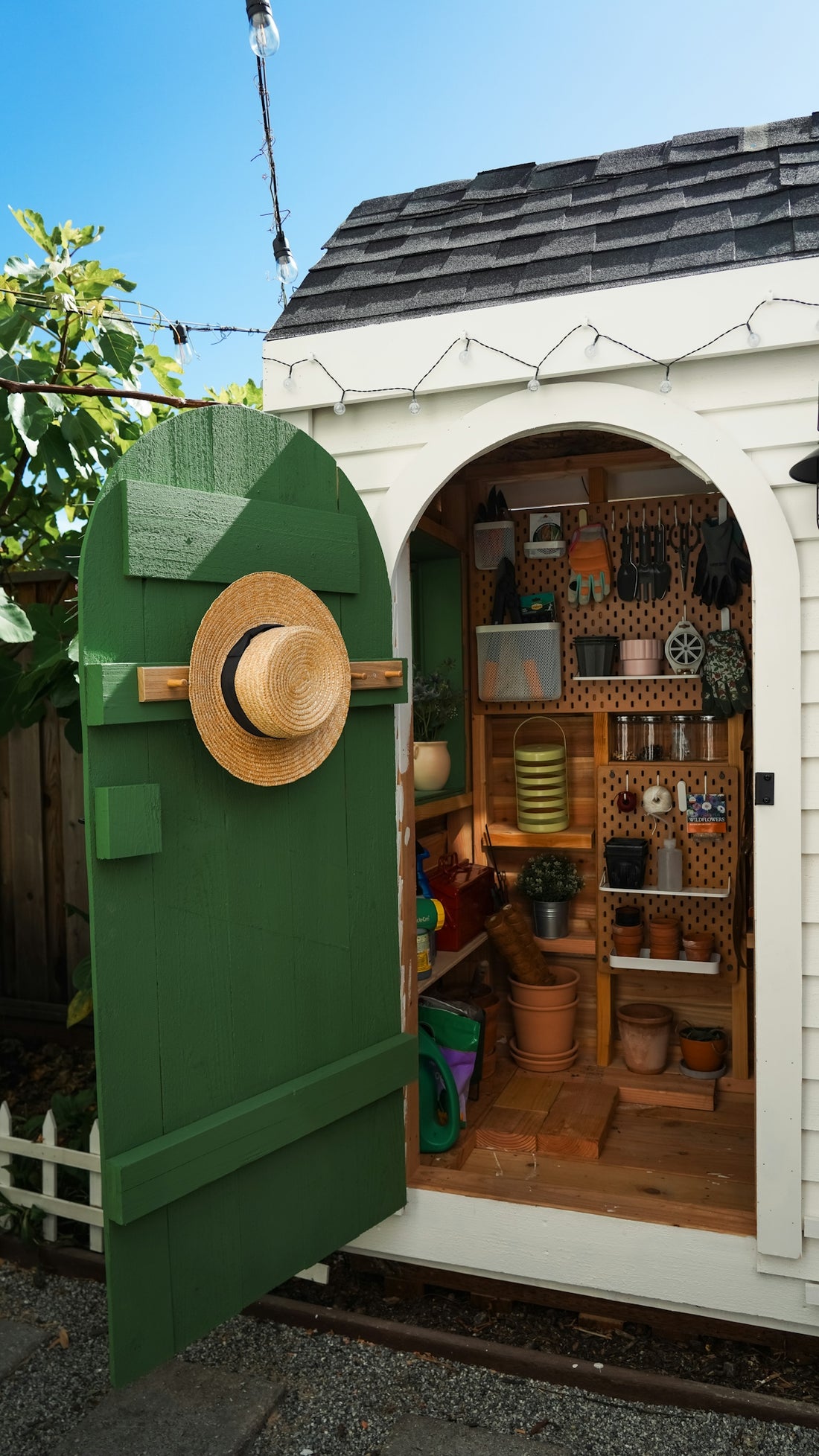 Open white garden shed with green door and gardening supplies